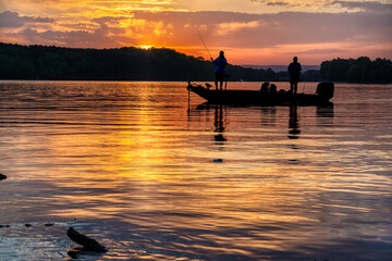 Two men bass fishing in a bass boat on Tims Ford lake in Tennessee with early morning sunrise...