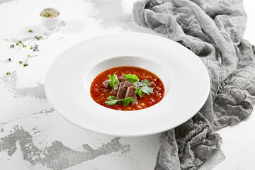 Authentic georgian beef soup Kharcho. Georgian lamb and rice soup. Caucasian dish - kharcho soup with rice, beef and coriander leaves. Kharcho in white plate on stone table.