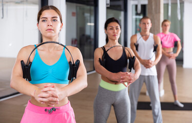 Sporty young woman doing fitness in the studio at a group training session performs an exercise with biceps working out, ..squeezing an isotonic ring between her hands