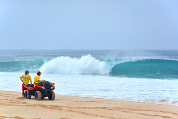 Ocean lifeguards patrolling the beach on an ATV under heavy surf looking for swimmers in distress on the northshore of Oahu in Hawaii - obrazy, fototapety, plakaty