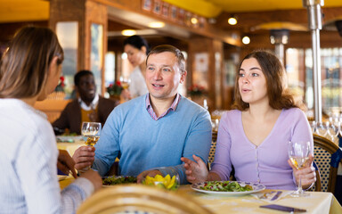 Positive couple enjoying dinner in restaurant. People sitting at served table, eating fresh vegetable salad and drinking wine..