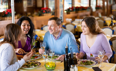 Cheerful adult people of different nationalities enjoying evening meal in restaurant. Friendly meeting over dinner with wine ..