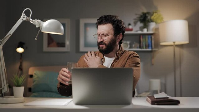 Shoulder pain. Bearded man in glasses working at computer is experiencing sharp pain in his shoulder. Middle aged worker with shoulder arthritis
