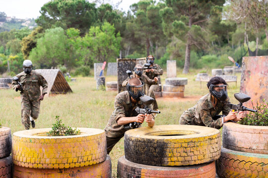 Expressive paintball team running with a marker guns at the open playing field