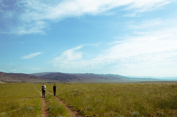 Fototapeta na wymiar Two travelers walk along the road among the green hills. Hiking in nature.