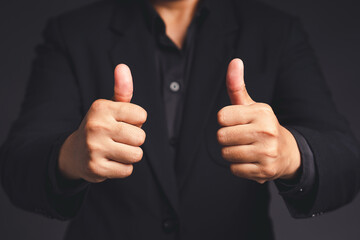 Businessman in a suit shows thumbs up with both hands while standing on gray background in the office