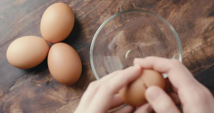 Female hand breaks an egg in glass bowl kitchen in top down close up