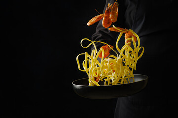 A professional chef prepares italian pasta with shrimp in a frying pan on a black background....