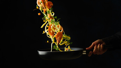 Appetizing Italian pasta with king prawns and vegetables in frozen flight on a black background....