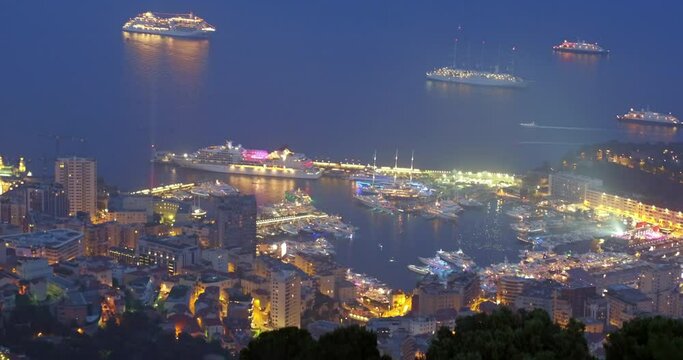 Aerial Shot Of Illuminated Harbor By Residential City, Drone Flying Backwards Over Graveyard At Night - Monaco