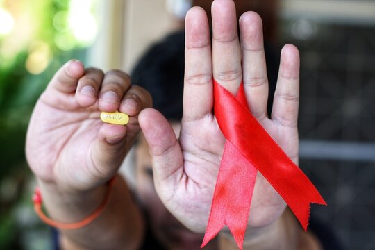 Young man show red ribbon and ARV pill in his hand,that's symbol of awareness and support for those living with HIV.World aids day and national HIV/AIDS or healthcare and medicine concept.