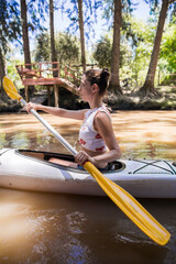 Side view of a young woman using a kayak paddle for a ride along river on summer afternoon. Healthy lifestyle concept. Copy space. Vertical.