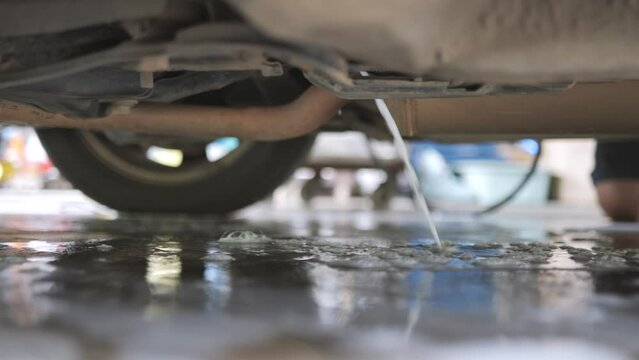 Water pouring under the car from spraying coil cleaner on the AC condenser. A deep cleaning process for air conditioner hygiene.