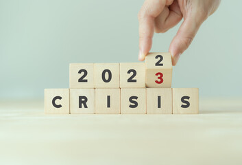 Crisis management concept in new year 2023 . Unexpected situation effects to business and life. Hand flips wooden cubes 2022 to 2023 with text "CRISIS" on beautiful grey background and copy space.