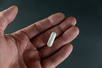 A man is holding a white medicine pill. The medicine lies in the open palm of an adult's hand. Health and Medicine.