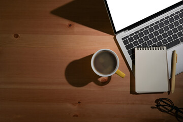 Office desk with laptop, blank notepad, coffee cup and glasses on wood table. Flat lay, top view, copy space.