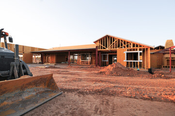 Wood-framed single-story building under construction with visible trusses and site grading,...