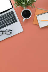 Computer laptop, cup of coffee, glasses and notebook on orange background. Top view.
