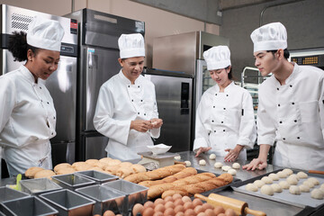 Multiracial professional gourmet team, four chefs in white cook uniforms and aprons knead pastry...