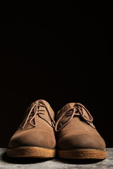 Men's suede brown low shoes with laces on a black background. Vertical copy space.