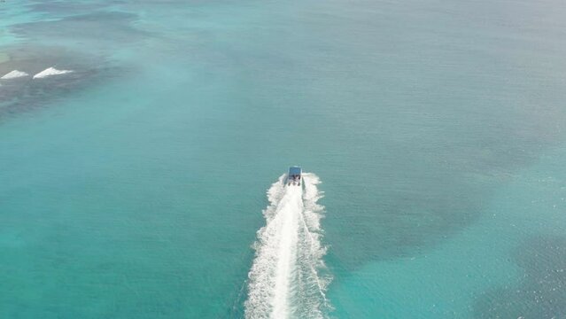 A large luxury powerboat cruises parallel along white sand beaches off Sana Island, aerial orbit