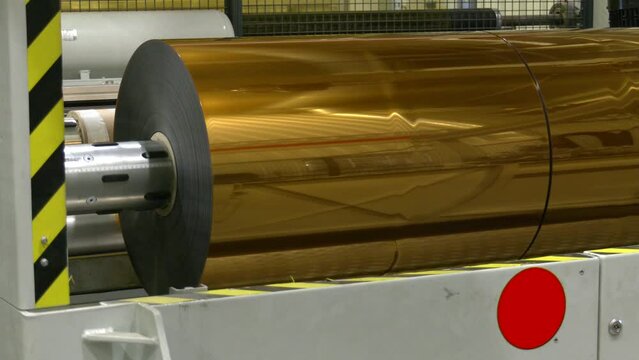 Moving roller with flat polyethylene gold film - automatic plastic bag making machine at exhibition. Recycling, manufacturing, industry, automated technology equipment concept