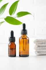 Natural beauty cosmetic product for skincare concept. Brown glass with dropper and organic green leaves on white background. Serum or essential oil with herbal extract. Branding mock-up. Copy space.