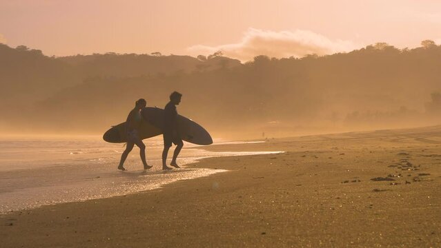 SLOW MOTION: Couple of surfers coming out of water after sunset surf session. Two friends after surf session in golden light at Playa Venao surf spot. Beach lifestyle shot in gorgeous light.
