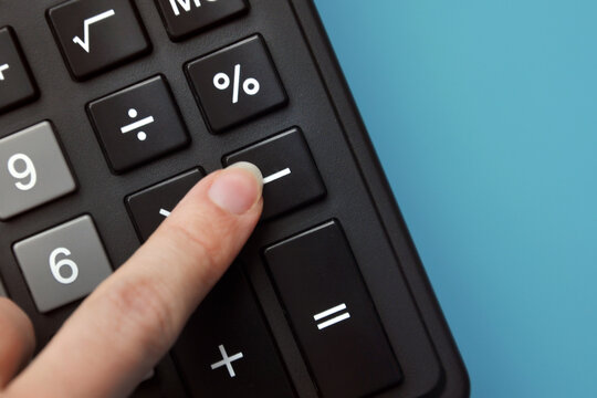 A person presses a minus sign on the calculator. A symbol for reducing something