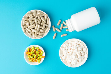 Blue background of large group of assorted capsules, pills and tablets in bottle and bowl