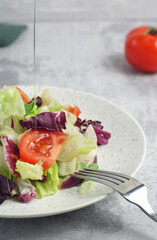 Tomato and lettuce salad in a plate on the table. Oil pouring from above