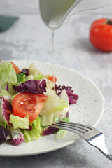 Tomato and lettuce salad in a plate on the table. Oil pouring from above