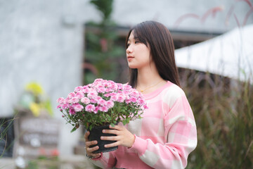 young Asian cute girl wearing pink shirt and holding beautiful pink flower, portrait female model with nature concept with pink flower in hand, happy and smile at outdoor