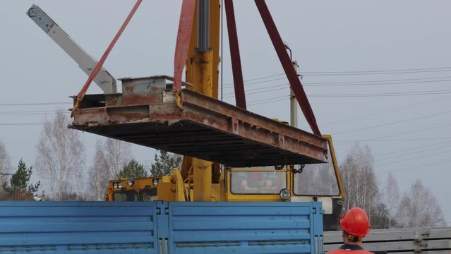 Slinger in helmet and vest supervises unloading at construction site. Real-time video. 4K resolution. White handyman unloads load.