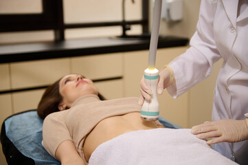 Close-up contact ultrasound sensor in the hand of a beautician giving cavitation body contouring, anti-cellulite slimming treatment in wellness spa