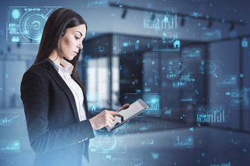 Attractive european businesswoman using tablet with abstract creative business charts and binary code hologram on blurry office interior background. 