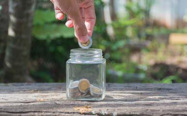 Hand holding coin and putting in glass bottle,save money concept,soft focus.