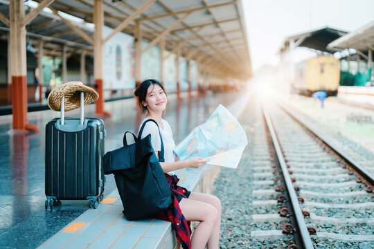 summer, relax, vacation, travel, portrait of a cute Asian girl looking at a map to plan a trip while waiting at the train station.