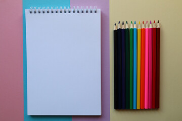 A clean white notebook and pencils on pink, blue and yellow background with space to copy.