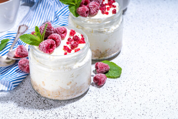 Overnight cheesecake oatmeal. Cheesecake morning breakfast layered parfafait dessert with homemade cottage cheese, mascarpone, oats and fresh raspberries, on sunny white concrete background copy space