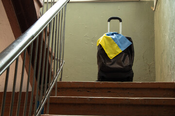 A suitcase with the flag of Ukraine stands in the entrance of the house, people leave their homes...
