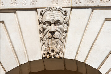 Brescia. Closeup of Medieval Broletto Palace (Palazzo Broletto or Palazzo del Governo), XII-XXI century. White stone arch with keystone and a gargoyle grotesque human mask. Lombardy, Italy, Europe.