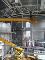 Scissor lift platform with hydraulic system elevated towards a factory roof with construction workers, Mobile aerial work platform