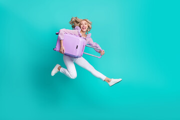 Photo of sweet adorable woman dressed purple blouse jumping high holding luggage isolated teal...