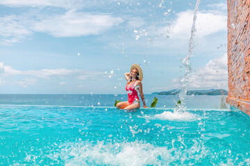 Woman in swimwear and straw hat relaxing in swimming pool at luxury hotel spa. Enjoying sea view of mediterranean travel holiday resort. Vacation in Thailand, Phuket, Asia.