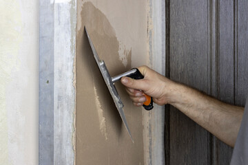 A worker applies plaster to a wall with a spatula.