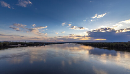 Obraz premium Evening landscape, sunset on the river. Wide river, horizon, clouds are reflected in the water. Sunlight through the clouds.