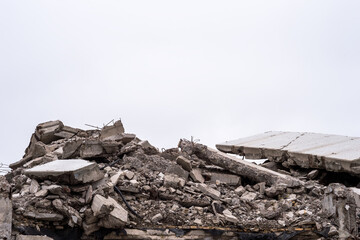 The remains of a destroyed building in the form of a pile of gray concrete debris and construction debris against a gray sky. Background - obrazy, fototapety, plakaty