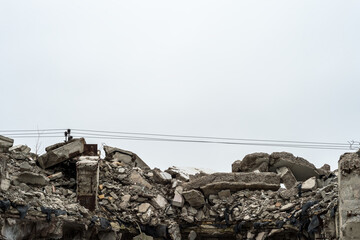 The remains of a destroyed building in the form of a pile of gray concrete debris and construction debris against the background of a power line and a gray sky. Background