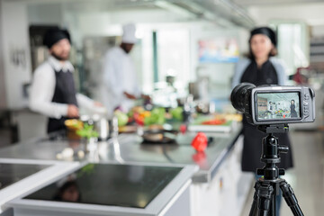 Selective focus of camera recording chefs in restaurant kitchen cooking gourmet dish for online...